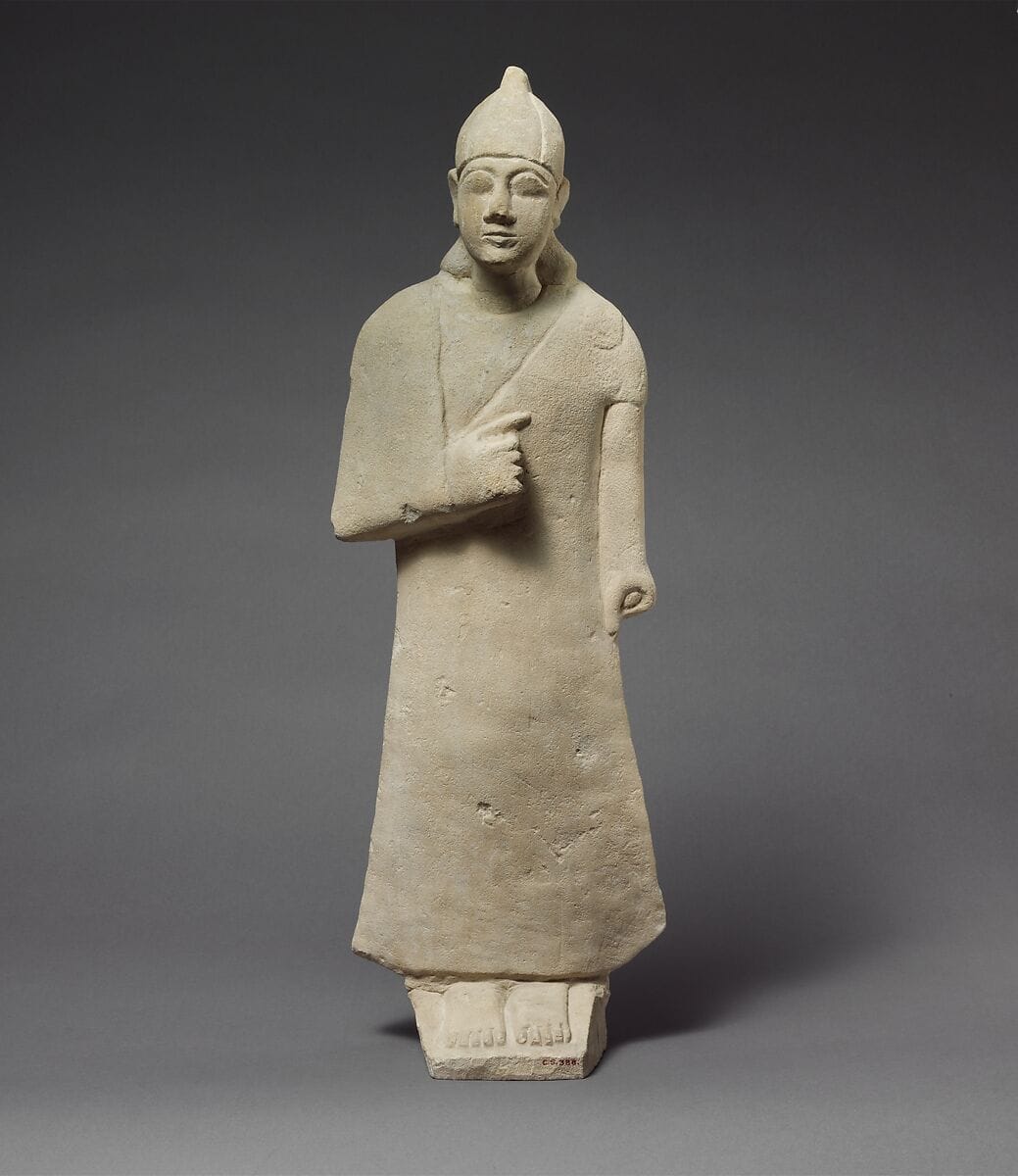 Statuette of a beardless male votary wearing a long garment and a conical helmet - image 1